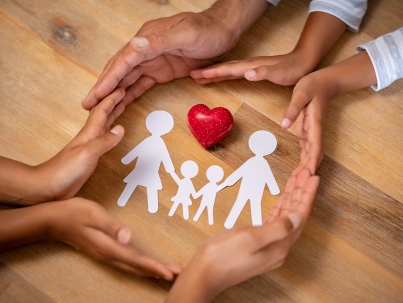 Close up hands of father, mother and daughters protecting family paper cutout with red heart. Hands of family with paper cutting and red heart shaped symbol stone. Unity, insurance and love concept.